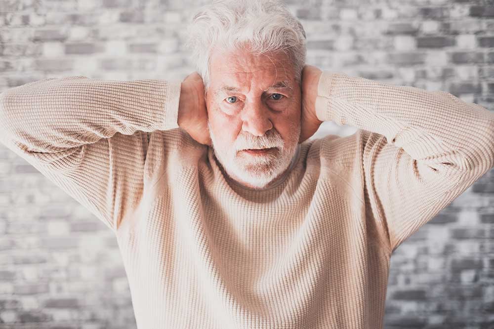 Older man with a white beard covering both ears as a clogged ear muffles sound, a concern Eastpoint Audiology evaluates in Louisville, KY